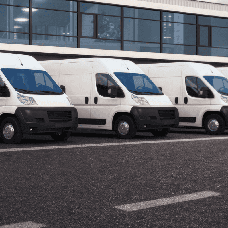 Row of white and blue commercial vans parked in line outside modern building, representing fleet washing and commercial vehicle cleaning services