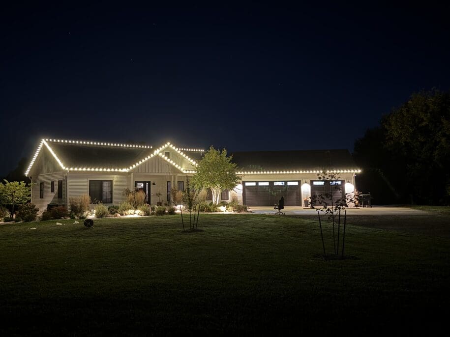 Beautifully lit ranch-style home at night in Fond du Lac, Wisconsin, featuring decorative white string lights outlining the roofline, three-car garage, manicured lawn, and landscaping