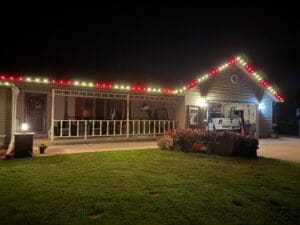 Mobile home at night decorated with red and white holiday lights along the roofline, with fall flower planters and RV in driveway in Fond du Lac, Wisconsin